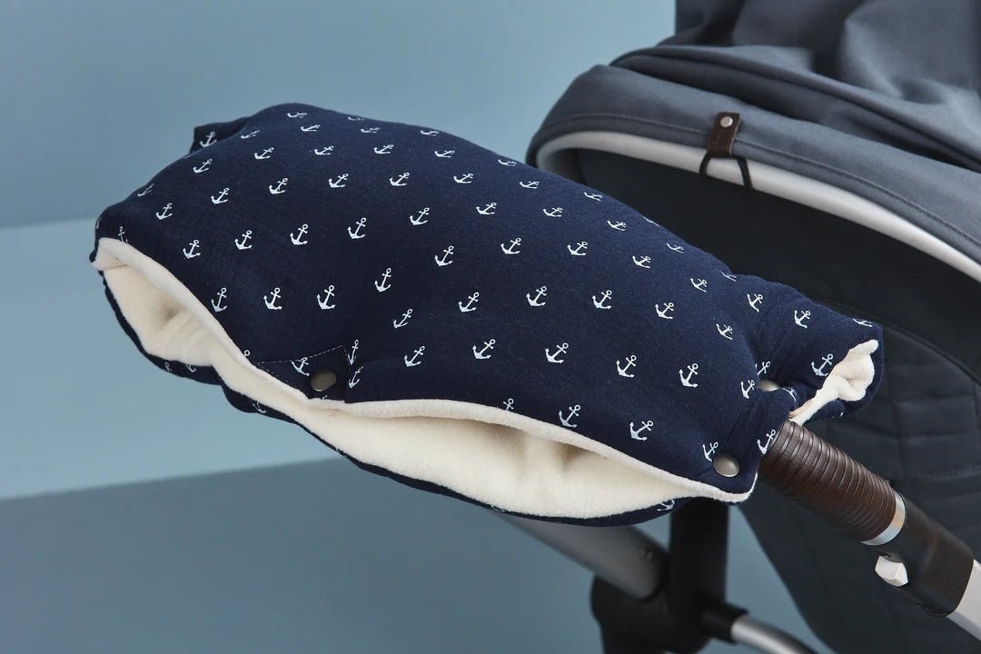 Nahaufnahme eines marineblauen Handsacks mit weißem Ankermuster, der an der Lenkstange eines Kinderwagens befestigt ist. Das Innenfutter ist weich und cremefarben.