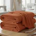 Zwei ordentlich gefaltete orangefarbene KraftKids Wandpaneel abgerundet Doppelkrepp-Stoffe liegen auf einem Holztisch mit Nähwerkzeugen und einem Maßband in der Nähe. Der sanft fokussierte Hintergrund schafft einen einladenden Raum für Wandgestaltungsprojekte.