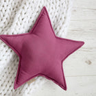 Das Sternkissen Leinen magenta dunkel von KraftKids ruht auf einer dicken weißen Strickdecke auf hellem Holz - ein idealer Akzent für jedes Kinderzimmer.