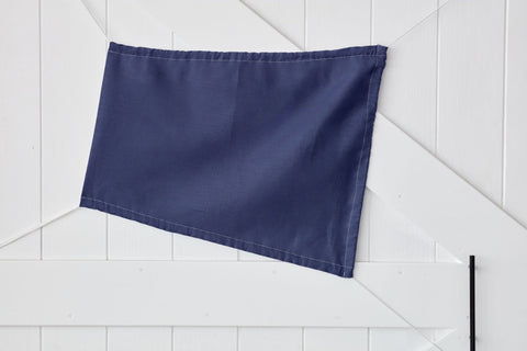 Ein KraftKids Sonnensegel Leinen blau dunkelblau, eine rechteckige Fahne aus 100% Leinen, ist schräg an eine weiße Holztafelwand gepinnt.