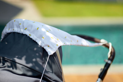 Eine Nahaufnahme des KraftKids Sonnensegel Musselin gelbe Zitronen Baldachin mit weißem Stoff und gelben Zitronen Druck, durch ein Schwimmbad mit grünem Gras-perfekt Sonnenschutz für Babys gezeigt.