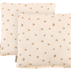 Zwei quadratische KraftKids Kissenbezüge Musselin Kirschen, cremefarben mit kleinen orangefarbenen und grünen Kirschenmustern, leicht überlappend, jeweils mit einem braunen Stoffanhänger an der Seite.