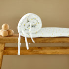 Eine aufgerollte KraftKids Bettumrandung Nestchen Musselin Kirschen mit kleinen gelben Mustern und Bindfäden sitzt auf einer Holzbank neben fünf natürlichen Holzkugeln, perfekt für Ihr Kinderbett.