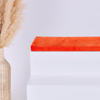 Eine hohe geflochtene Vase mit Pampasgras steht neben einem weißen Stufenpodest, auf dem die KraftKids GmbH Sitzauflage für Ikea TROFAST Cord Breitcord Orange Reinorange steht, alles vor einem schlichten weißen Hintergrund.