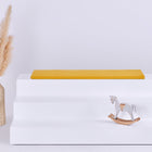 Ein weißer, dreistöckiger Aufsteller mit einer KraftKids GmbH Sitzauflage für Ikea TROFAST Doppelkrepp Gelb Senf auf der oberen Etage, einer dekorativen Vase mit getrocknetem Pampasgras auf der linken Seite und einem kleinen Holzschaukelpferd auf der unteren Etage.