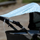 Nahaufnahme eines Kinderwagens mit dem KraftKids Sonnensegel "weiße Pfeile auf Blau" als Schattenspender drapiert. Perfekt für optimalen Sonnenschutz des Babys beim Spaziergang im Freien an einem sonnigen Tag.