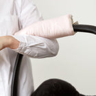 Eine Person in einem weißen Hemd stützt ihren Arm auf einen Kinderwagengriff, der mit der KraftKids Armschoner Babyschale weiße Halbkreise auf Pastelrosa mit sicherem Klettverschluss bedeckt ist. Der Hintergrund ist einfarbig und hell.