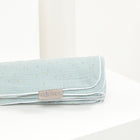 Eine gefaltete grüne Babydecke Musselin mit goldenen Punkten und einem KraftKids-Etikett ruht auf einer weißen Oberfläche - die perfekte Baumwolldecke für Ihr Kind.