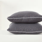 Zwei Kissenbezüge Musselin goldene Punkte auf Grau von KraftKids, mit kleinen goldenen Punkten und weißer Paspel, sind auf einer weißen Fläche gestapelt und verleihen Ihrer Bettwäschekollektion vor einem hellen Hintergrund Eleganz.