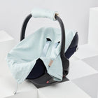 Eine grüne Babydecke für Babyschale Sommer mit goldenen Punkten aus Musselin von KraftKids liegt in einer Babyschale mit gepolstertem Griff und Drei-Punkte-Gurt-System auf weißen, geometrischen Plattformen.