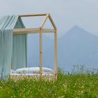 A Bettbaldachin Musselin mint Pusteblumen von KraftKids steht inmitten einer Wiese mit Wildblumen, vor malerischer Bergkulisse und bewölktem Himmel-eine traumhafte Inspiration für die Kinderzimmer Dekoration.