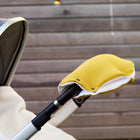 Nahaufnahme eines grau-weißen Kinderwagens mit dem KraftKids Kinderwagenmuff Doppelkrepp Gelb Senf aus weichem Vlies, der am Lenker befestigt ist. Im Hintergrund ist ein Holzzaun zu sehen.