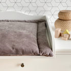 Eine kuschelige, graue Wickelauflage Cord Breitcord Grau von KraftKids steht auf einer weißen Kommode neben geflochtenen Körben und Holzklötzen vor einer geometrischen Wand - der perfekte Wickelplatz.