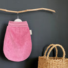 Der KraftKids Strampelsack Frühling Sommer Cord Breitcord Rosa hängt an einem natürlichen Holzast an einer schwarzen Wand. Darunter und rechts daneben steht ein geflochtener Strohkorb mit zwei Griffen.