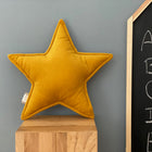 Ein KraftKids Sternkissen Cord Breitcord Gelb Senf sitzt auf einem Holzwürfel an einer grauen Wand, neben einer Tafel mit handgeschriebenen Buchstaben A-E in weißer Kreide - ein reizvoller Akzent für jedes Kinderzimmer.