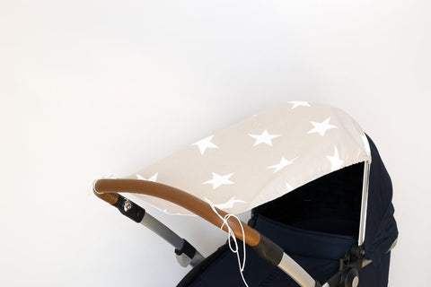 Eine Nahaufnahme des KraftKids Sonnensegels große weiße Sterne auf Beige mit einem beigen Verdeck mit großen weißen Sternen auf einem Kinderwagen mit braunem Griff hebt sich von einem schlichten weißen Hintergrund ab.