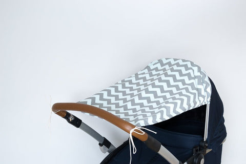 Nahaufnahme eines Kinderwagens mit einem KraftKids Sonnensegel Chevron hellgrau und mint als Sonnenschutz und einem braunen Lenker, vor einem schlichten weißen Hintergrund.
