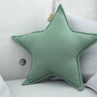 Das KraftKids Sternkissen Doppelkrepp Grün Jade liegt auf einem grauen Sofa mit hellgrauen Kissen vor einer Betonwand - ein ideales Accessoire fürs Kinderzimmer.