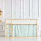 Ein minimalistisches Interieur zeigt ein kleines hölzernes Hochbett, das mit KraftKids Hochbettvorhänge Set 2+1 Musselin goldene Punkte auf Grün für das Kura-Bett geschmückt ist, sowie eine gewebte Vase mit Pampasgras und zwei Holzwürfel vor einer weiß getäfelten Wand.